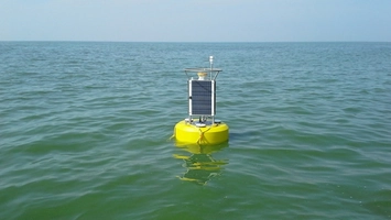 Yellow water quality monitoring buoy with solar panel on open water