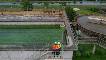 Engineers in hi-vis gear on a walkway above green-water settling tanks at an outdoor water treatment facility