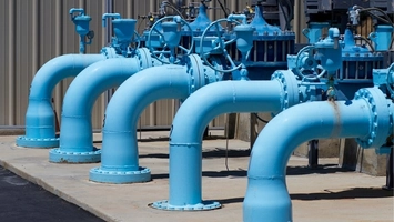 Blue water distribution pipes and valve assemblies mounted at an outdoor municipal utility pumping station