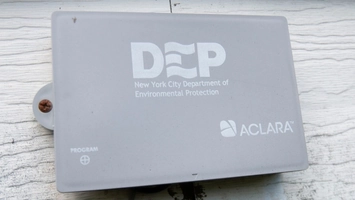 Aclara device branded with New York City Department of Environmental Protection text on white timber siding